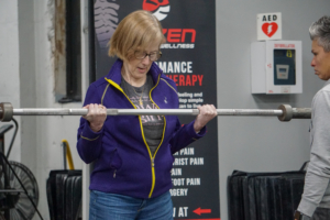 Mary is lifting a weighted bar during the 8035 Adaptive Fitness program.